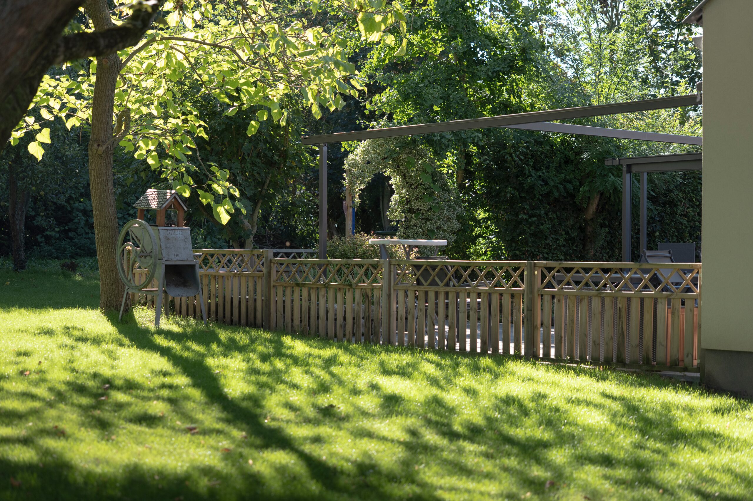 Clôture en bois à croisillons délimitant une terrasse dans un jardin ombragé