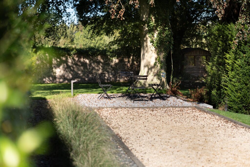 Terrain de pétanque et coin détente sous un grand arbre, devant un mur en pierre
