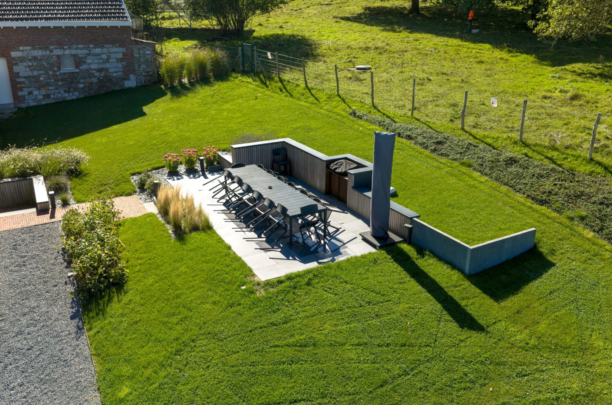 Terrasse en dalles avec grande table, cuisine extérieure et cheminée au milieu de la pelouse