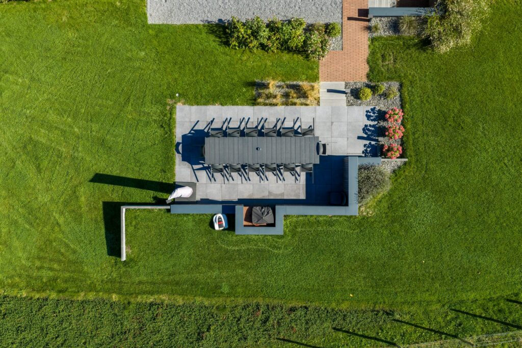 Vue aérienne d'une terrasse en dalles grises avec grande table, entourée de pelouse